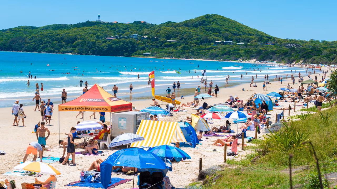 Swimmers and longboarders at Main Beach Byron Bay with the cape in the background