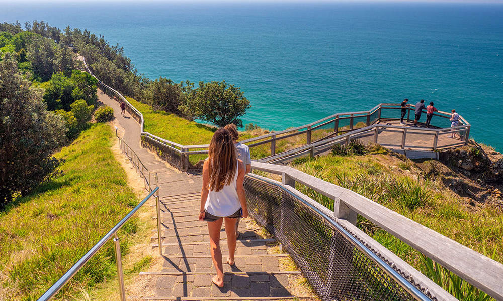 Walkers on the boardwalk approaching Cape Byron Lighthouse above the Pacific Ocean