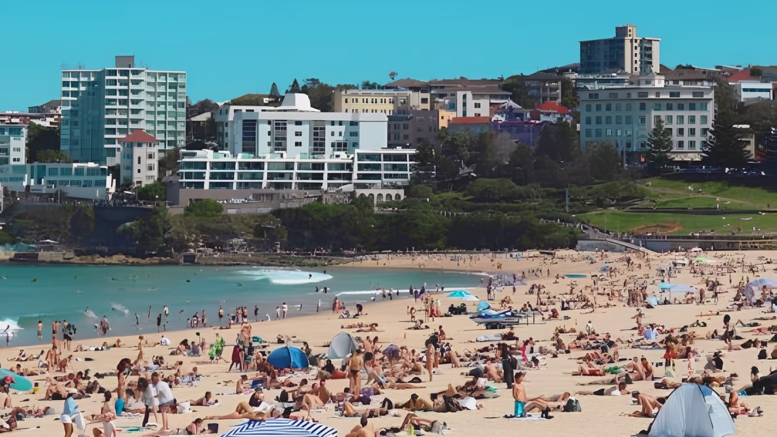 Bondi Beach, Sydney, on a clear summer day with swimmers in the surf and the clifftop walk behind