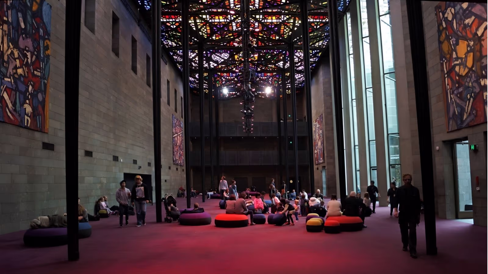 Visitors lying on the floor of the NGV Great Hall in Melbourne beneath Leonard French’s stained-glass ceiling