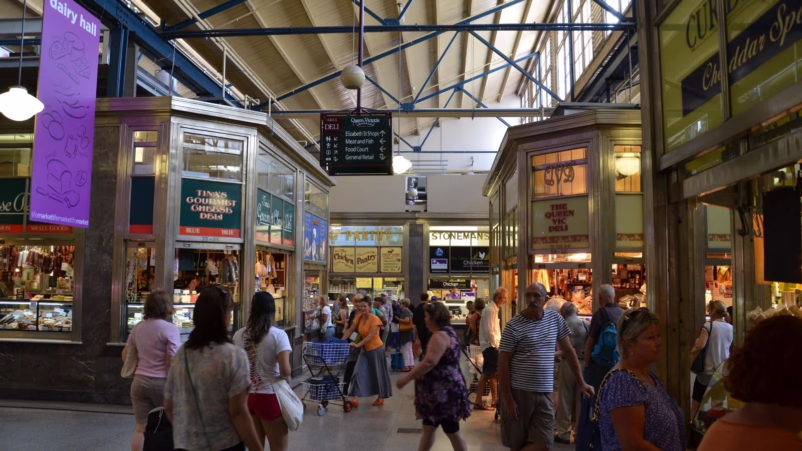 Traders and shoppers in the Deli Hall at Queen Victoria Market Melbourne, with cheese, charcuterie and fresh produce stalls